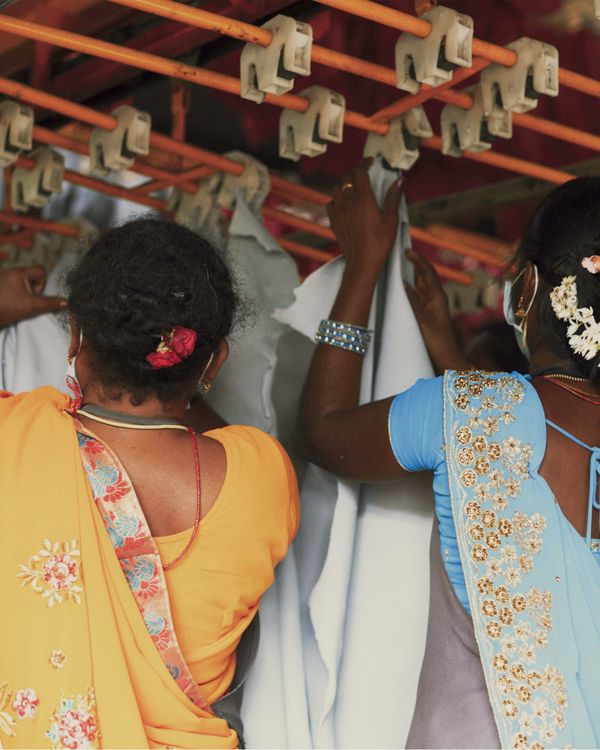 Two Indians women are standing back to the camera and picking up pieces of leather from a drying rack.