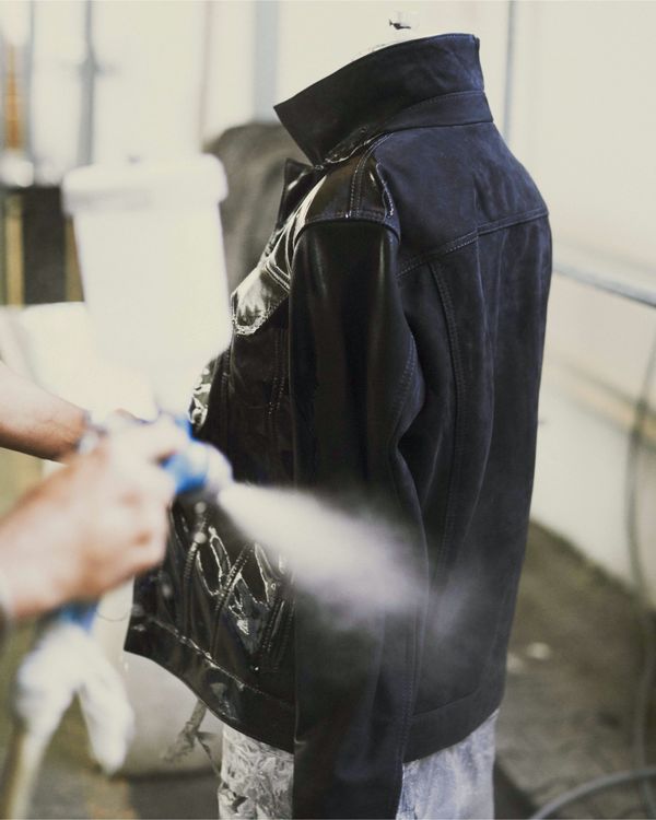 A jacket is on a wood mannequin and a man is applying the last treatment to reveal our signature finitions. 