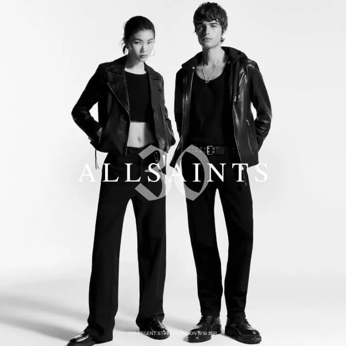 Black and white photograph of a female and male model standing next to each other wearing AllSaints clothes.