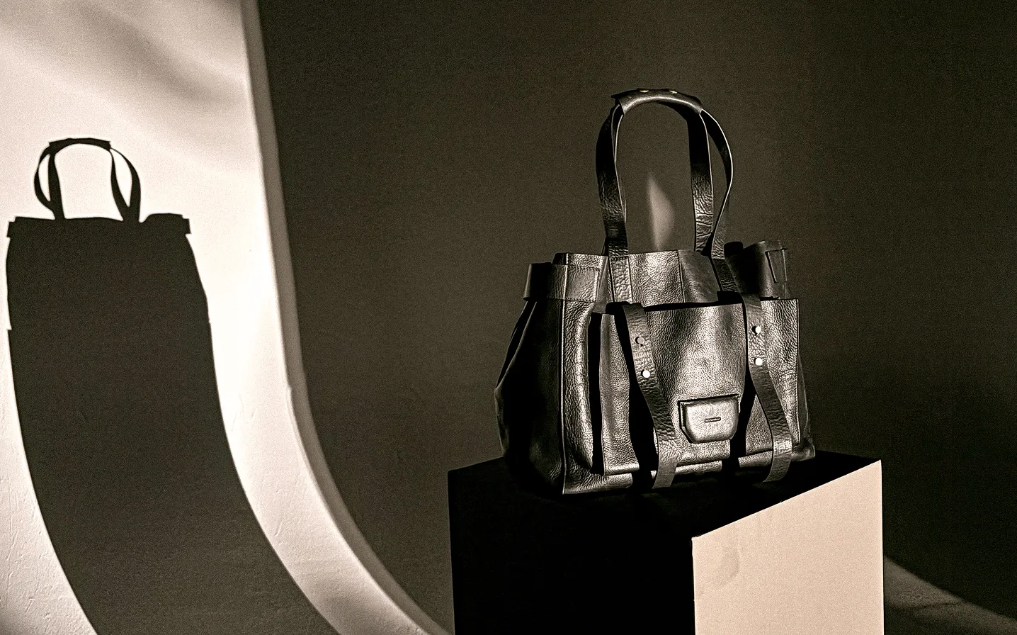 A black leather handbag stood on a stand with its shadow reflecting in the background