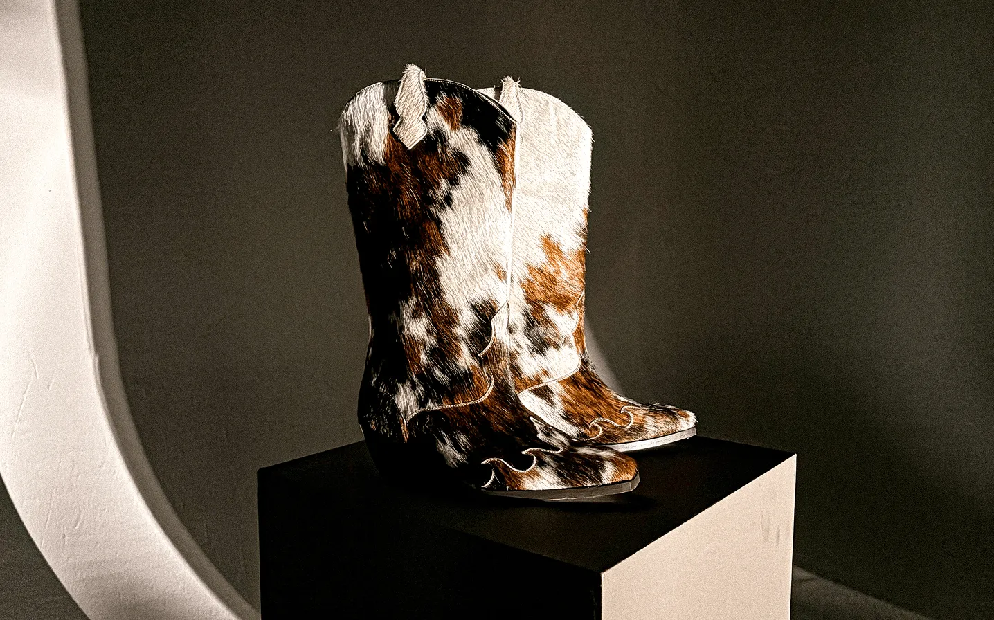 A pair of cow hide western style boots on a stand in front of a grey background
