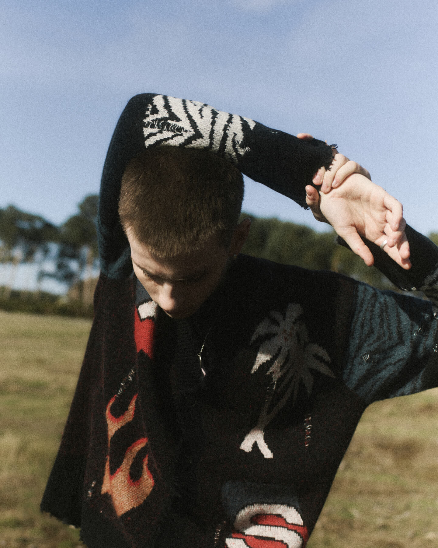 Man wearing black flame and animal print cardigan in a field