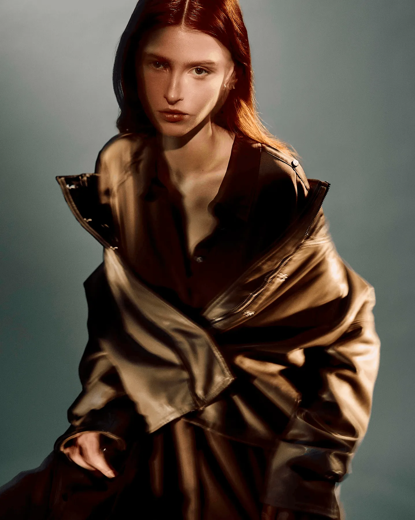 Woman wearing an open leather jacket sitting in front of a grey background