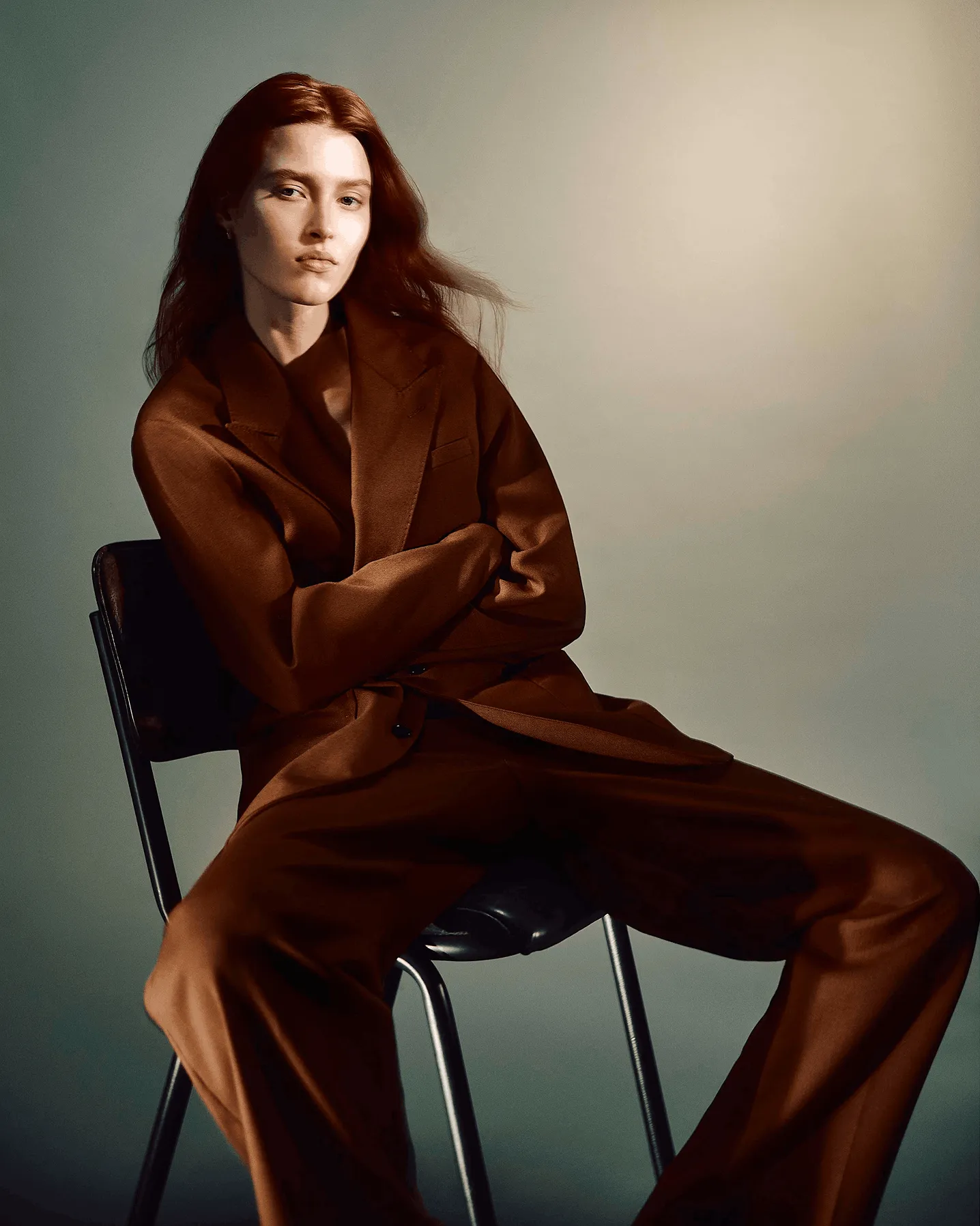 Women sitting on a black chair wearing a brown suit with a grey background