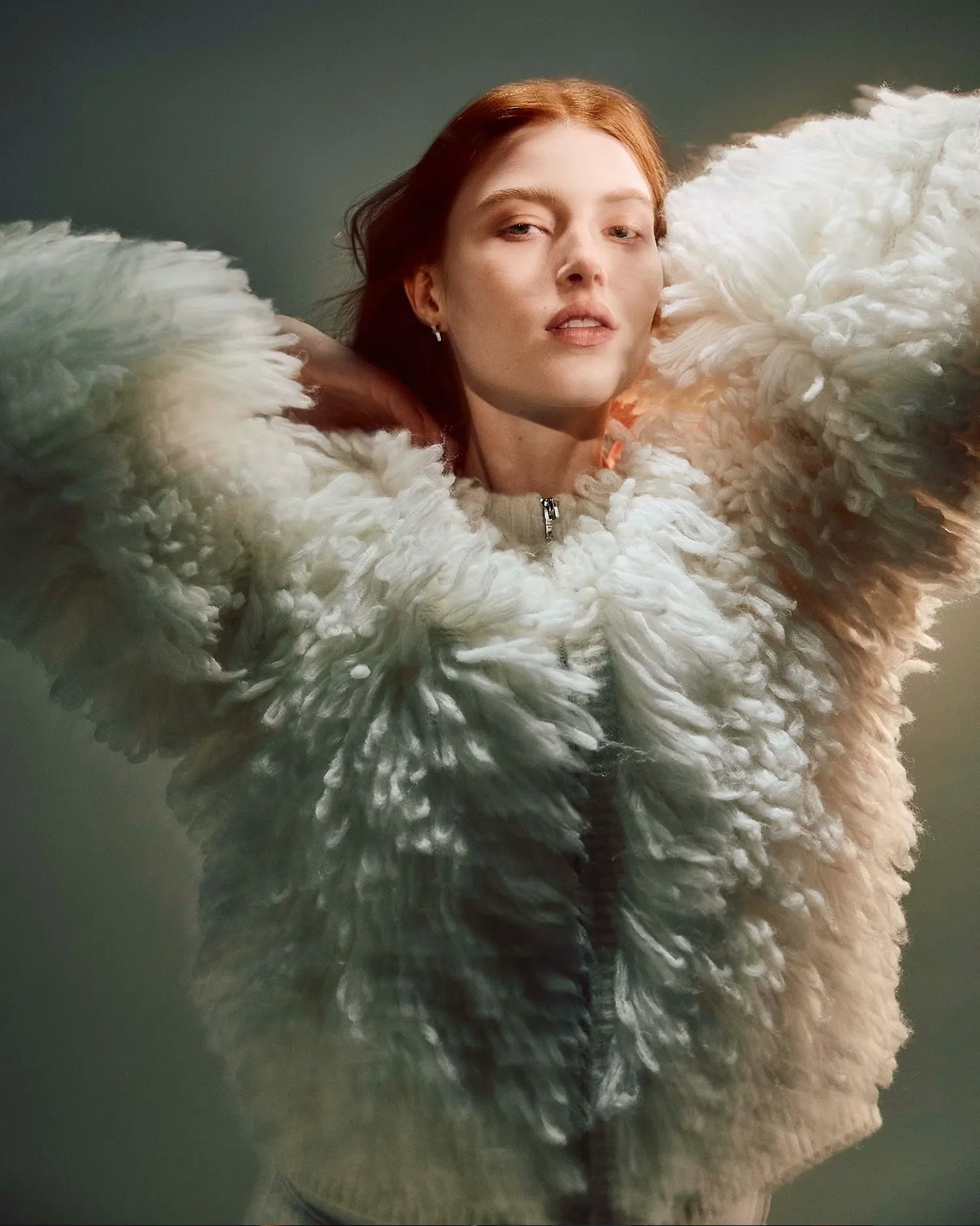 Woman wearing an open leather jacket sitting in front of a grey background