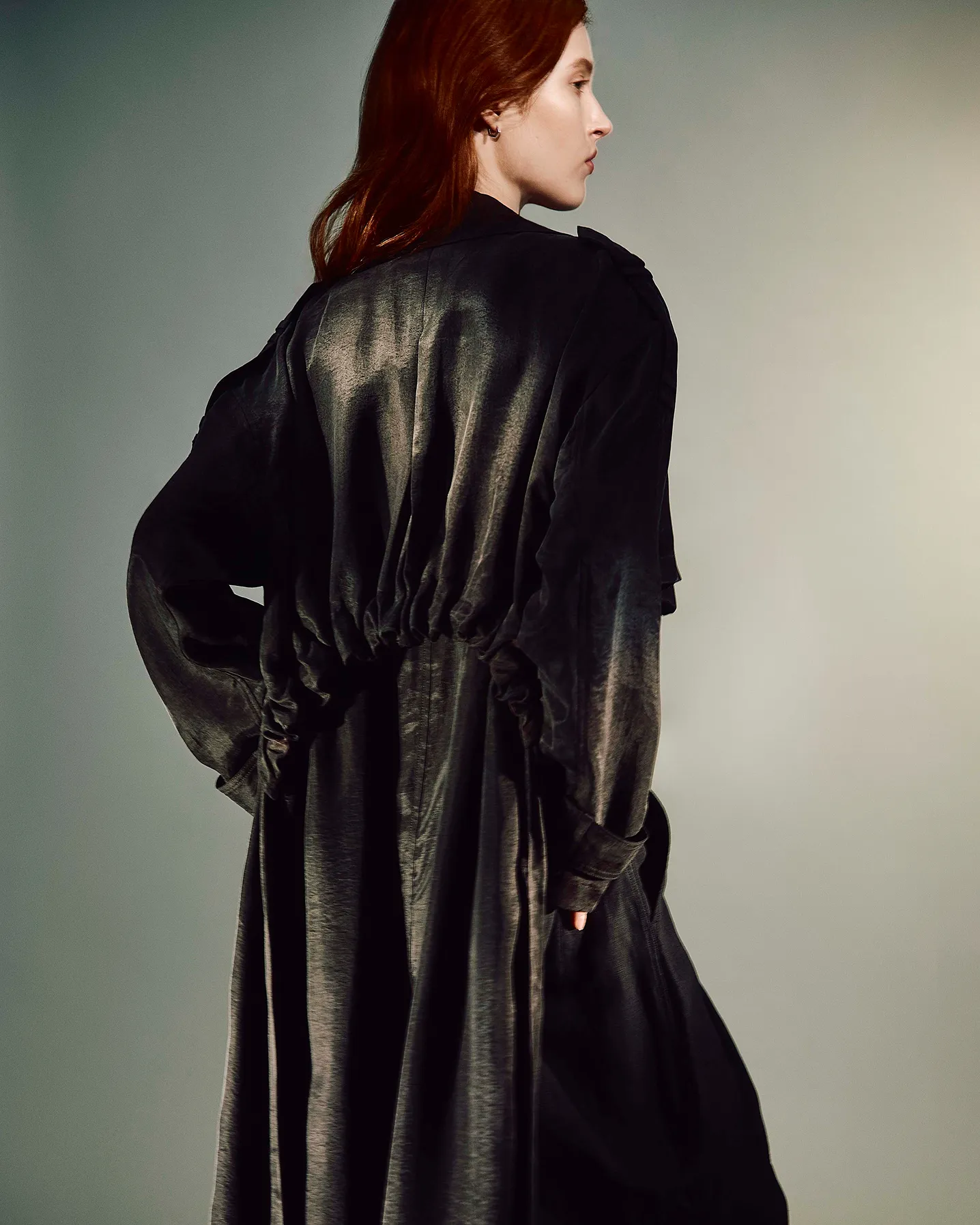 Women facing away from the camera wearing a black trench coat with a grey background