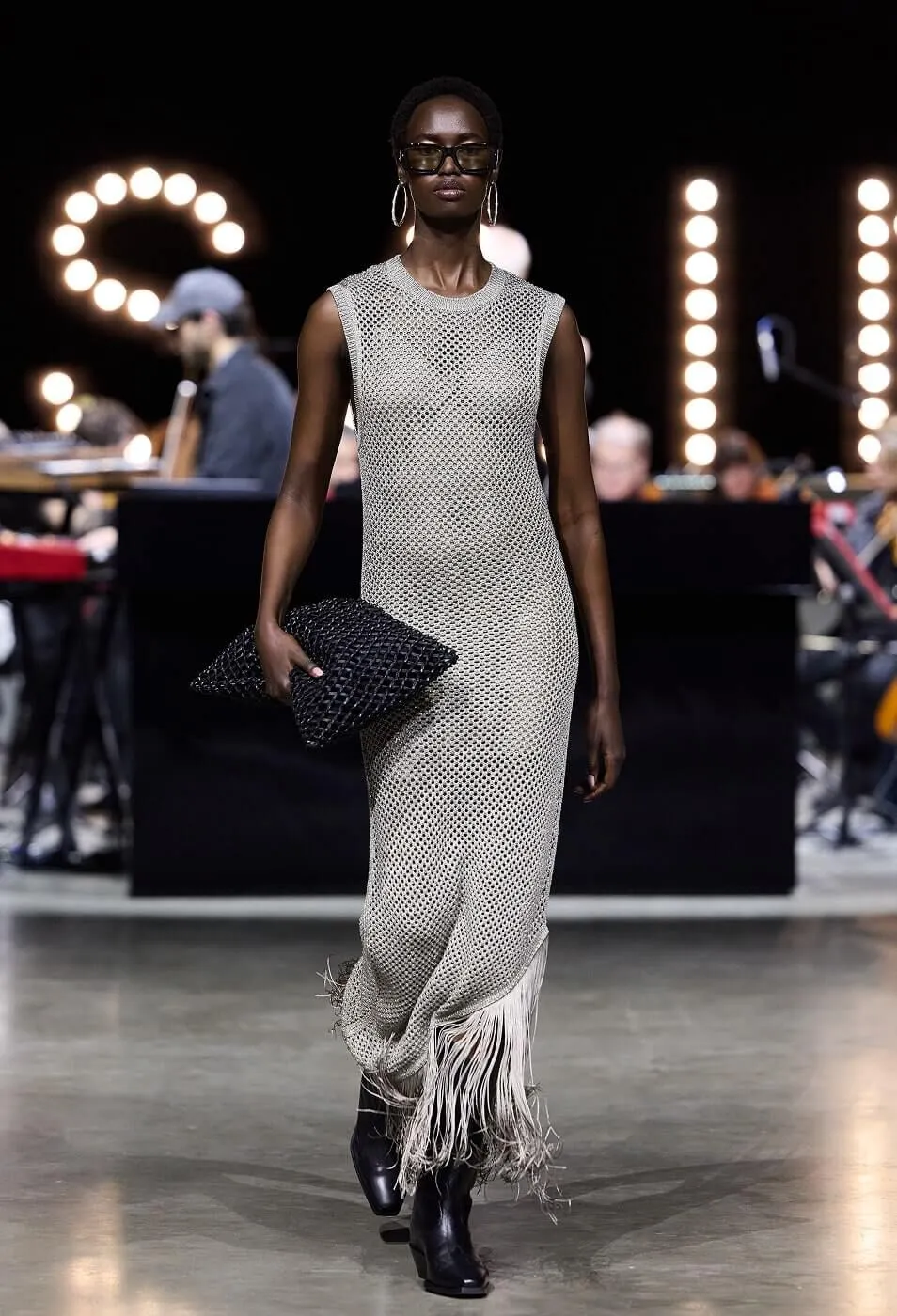 Woman wearing metallic knitted dress with fringe and a black clutch bag