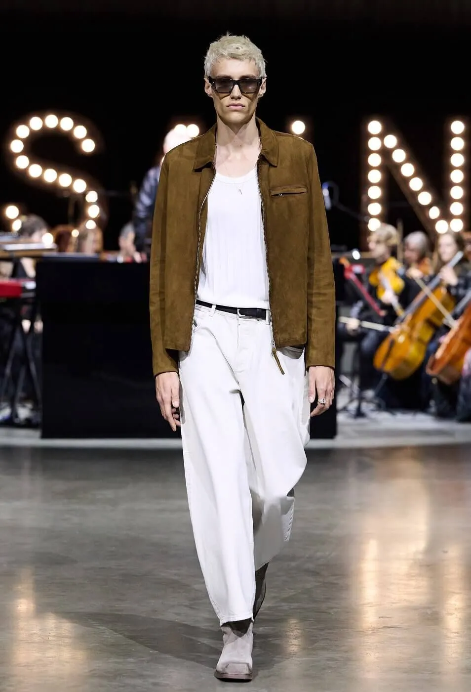 Man wearing brown suede jacket with white tank top and white trousers