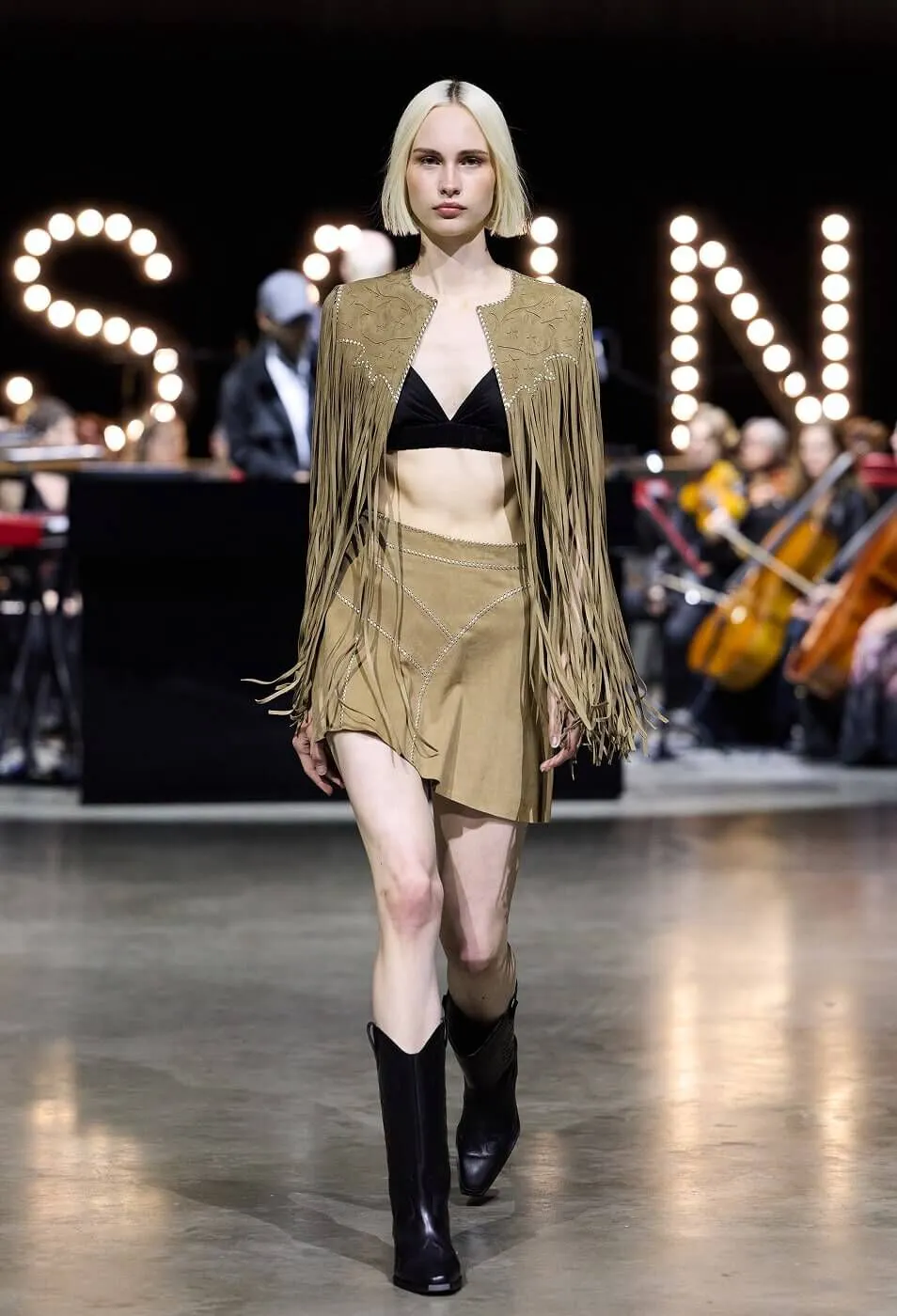 Woman wearing tan fringed jacket with matching skirt and black boots