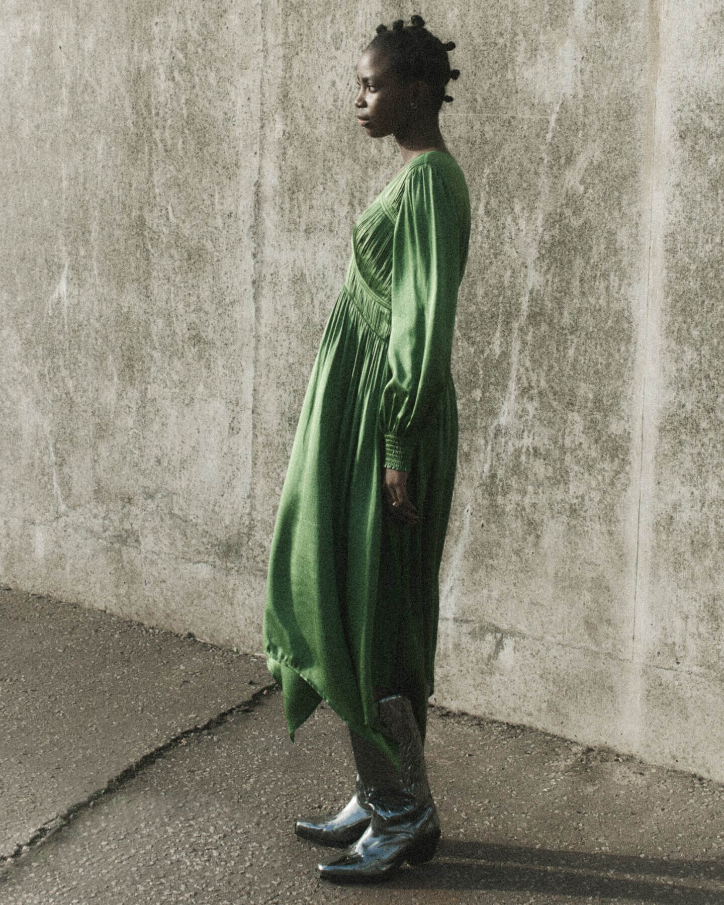 Woman wearing a long green dress and metallic leather cowboy boots standing in front of a wall