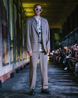 A man wearing a grey suit over a patterned shirt catwalking.
