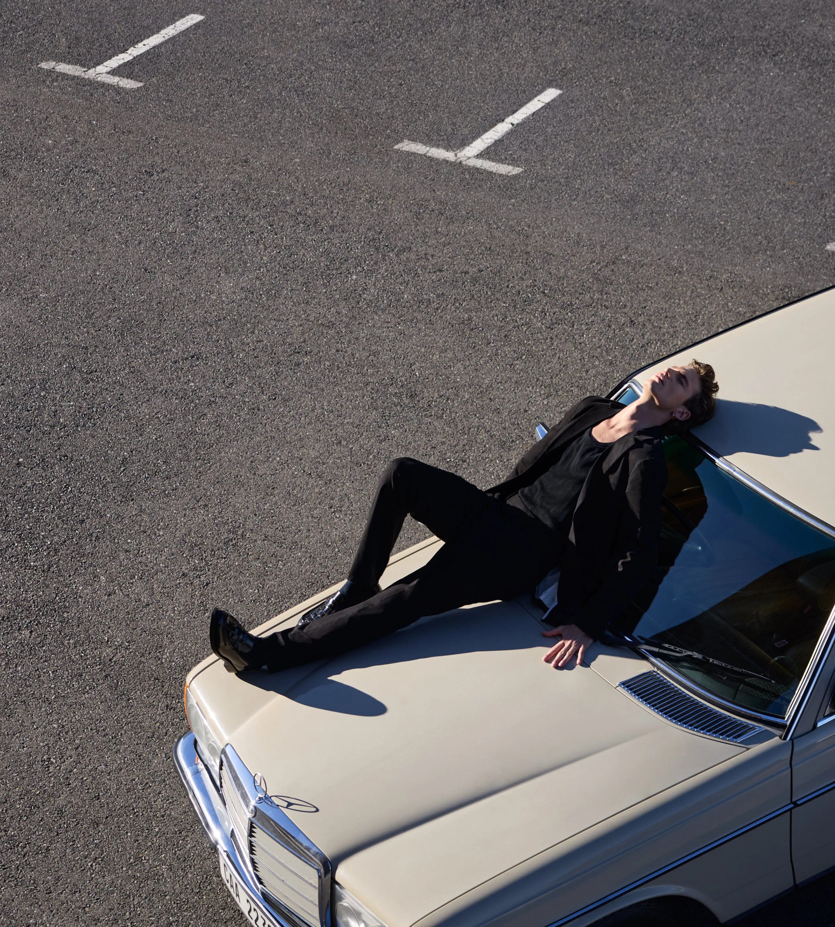 Photograph of a male model sitting on a car.