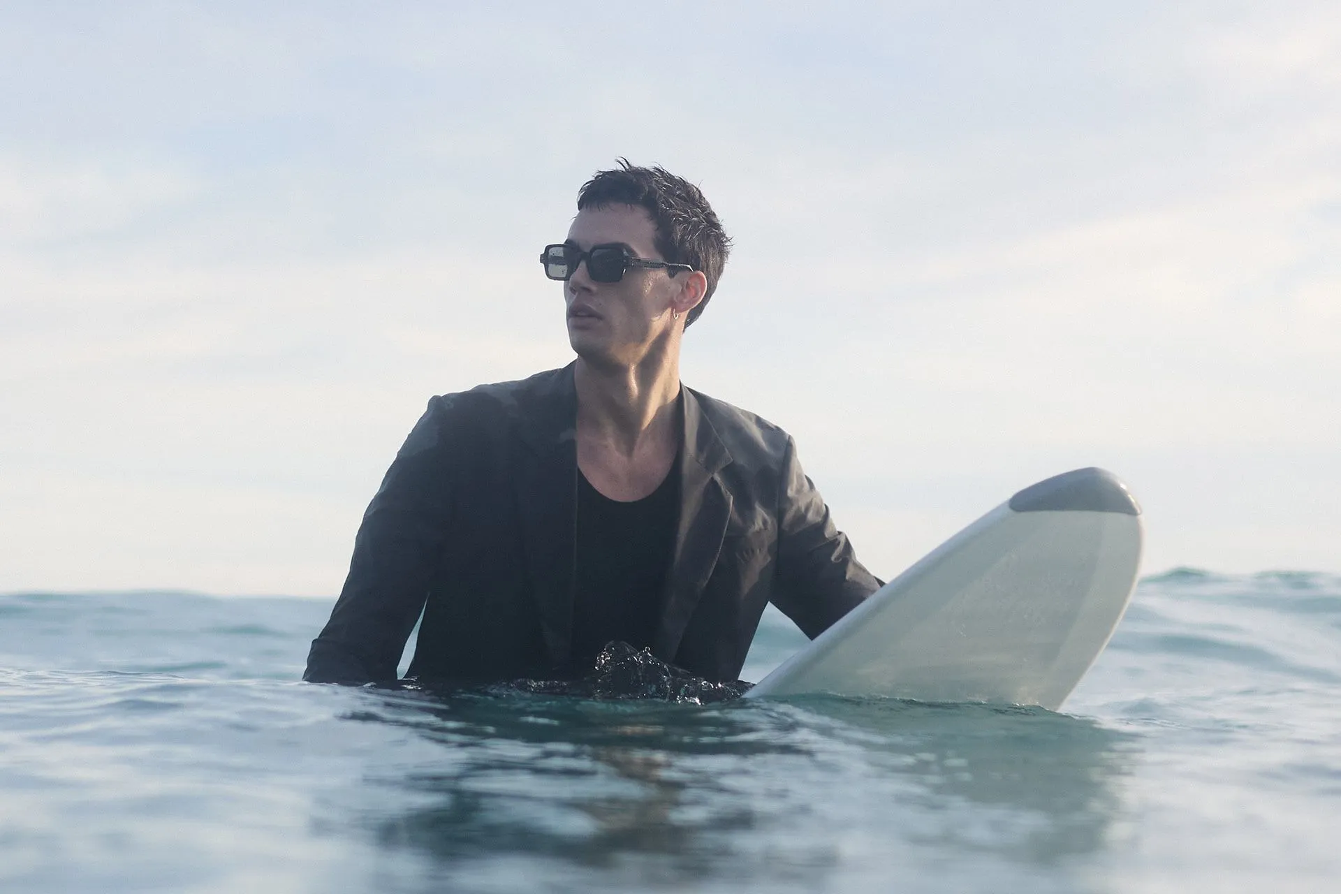 Male model in a suit on a surfboard in the sea.
