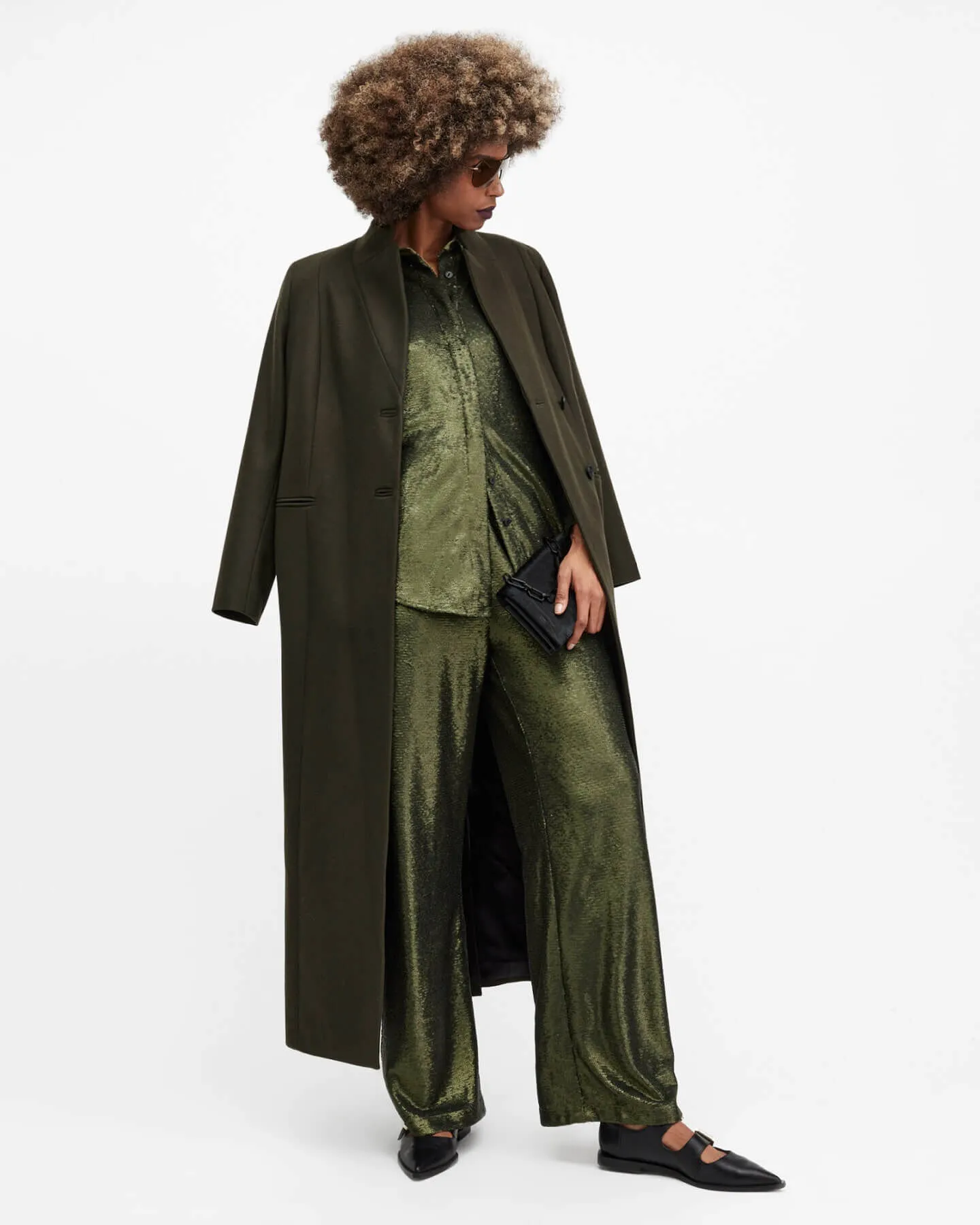 Woman wearing a green metallic blouse trousers and green coat.