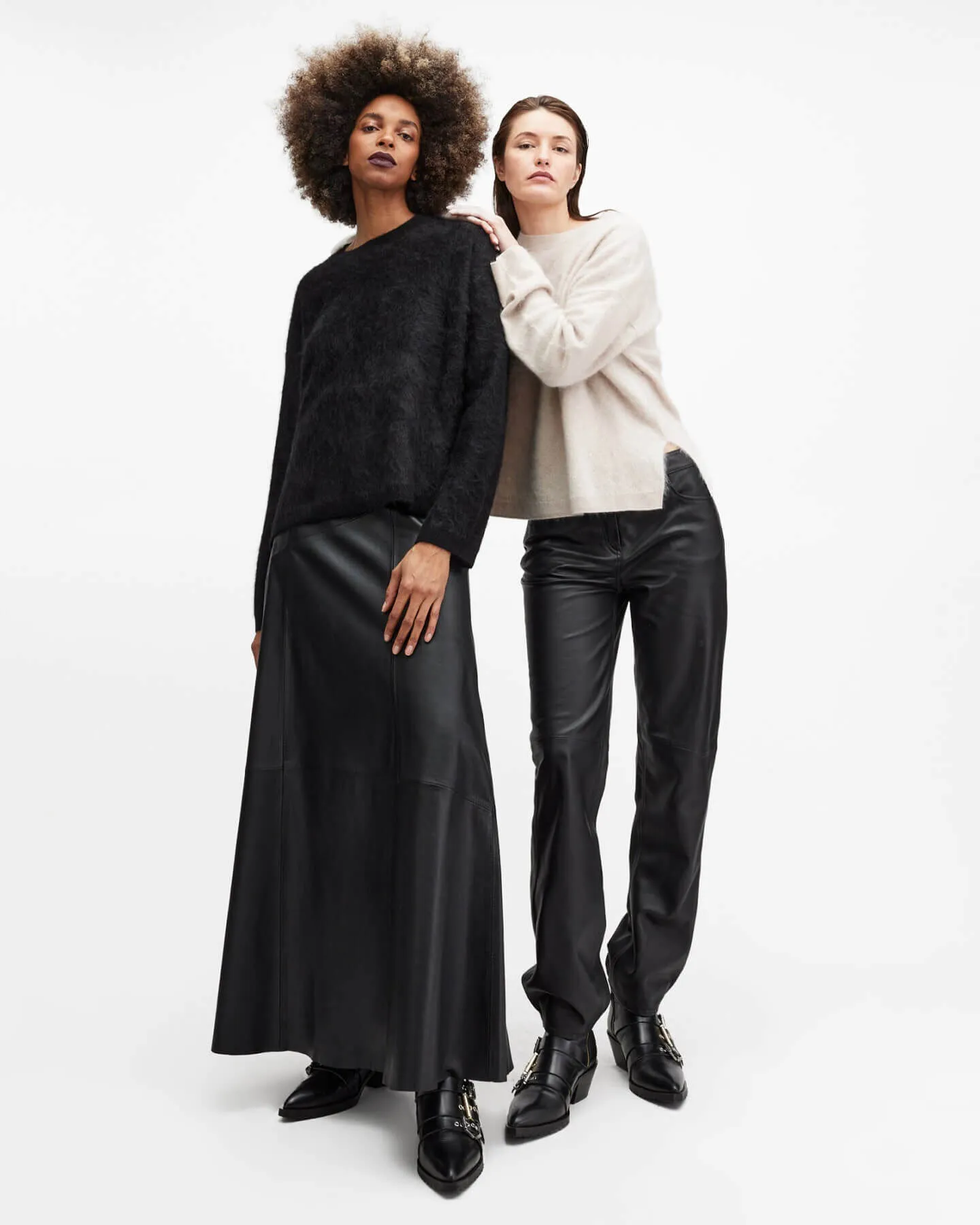 Two women one wearing a white jumper and black skirt and the other wearing white jumper and black trousers.