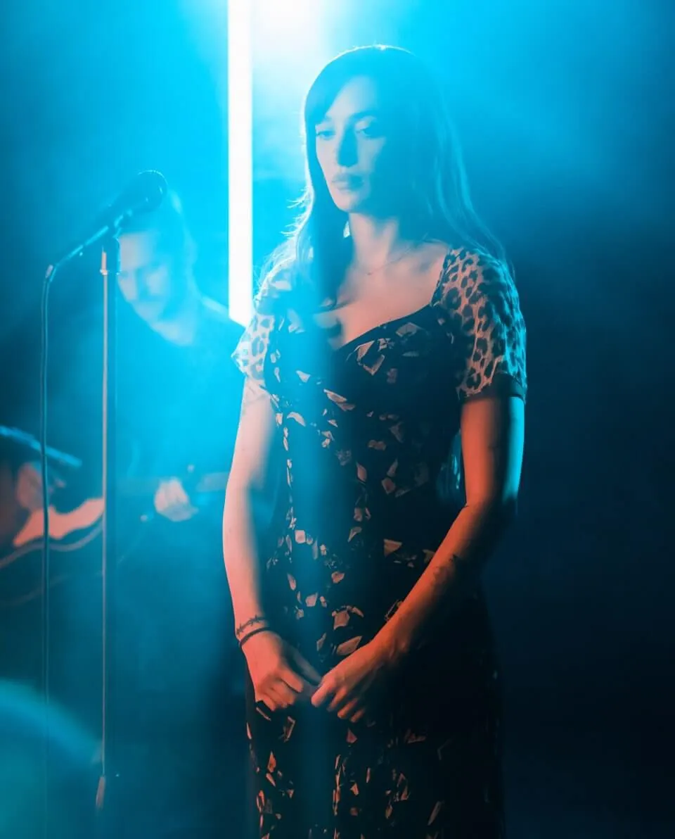 Olivia OBrien standing under blue light.